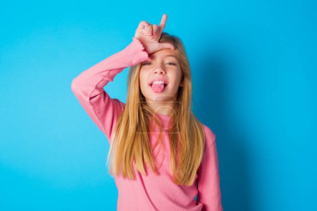 Photo for Funny pretty teen girl makes loser gesture mocking at someone sticks out tongue making grimace face. - Royalty Free Image