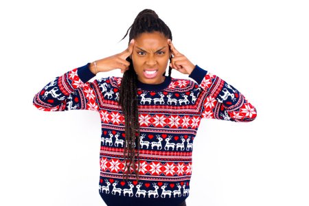 Photo for African American woman wearing Christmas sweater against white wall concentrating hard on an idea with a serious look, thinking with both index fingers pointing to forehead. - Royalty Free Image