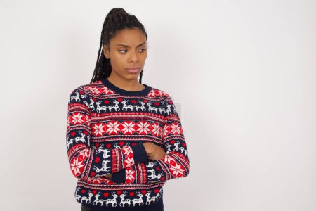 Photo for Displeased African American woman wearing Christmas sweater against white wall with bad attitude, arms crossed looking sideways. Negative human emotion facial expression feelings. - Royalty Free Image