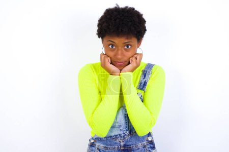 Foto de Retrato de la triste joven afroamericana con el pelo corto con denim en general contra la cara de las manos blancas de la pared - Imagen libre de derechos
