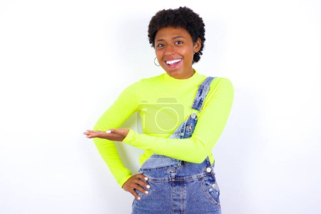 Foto de Joven mujer afroamericana con denim en general dice: wow lo emocionante que es, ha sorprendido a la expresión, muestra algo en el espacio en blanco con la palma. Concepto de publicidad. - Imagen libre de derechos