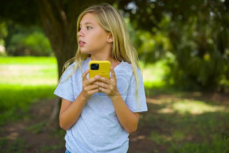 Téléchargez les photos : Très ennuyé jolie fille tenant smartphone dans le parc - en image libre de droit