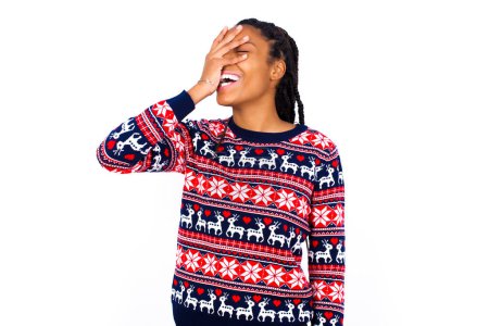 Photo for Charismatic carefree joyful African American woman wearing Christmas sweater against white wall likes laugh out loud not hiding emotions giggling hear funny hilarious joke chuckling facepalm. - Royalty Free Image