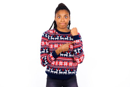 Téléchargez les photos : Femme afro-américaine portant un pull de Noël contre un mur blanc pressé pointant vers regarder le temps, l'impatience, bouleversé et en colère pour retard de délai - en image libre de droit