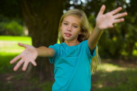 Porträt eines schönen kaukasischen kleinen Mädchens mit blauem T-Shirt, das draußen im Park steht