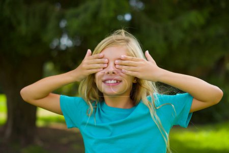 Photo for Portrait of beautiful caucasian little kid girl wearing blue t-shirt standing outdoor in the park hide face with hands - Royalty Free Image