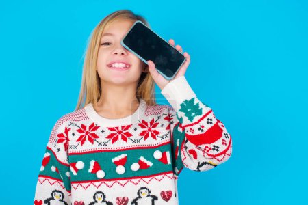Photo for Pretty girl holding modern smartphone covering one eye while smiling - Royalty Free Image