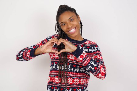 Photo for African American woman wearing Christmas sweater against white wall smiling in love showing heart symbol and shape with hands. Romantic concept. - Royalty Free Image