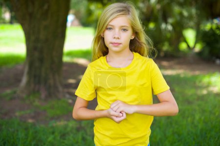 Foto de Foto de alegre niña caucásica confiada usando camiseta amarilla de pie al aire libre brazos juntos - Imagen libre de derechos