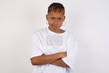 Photo for Picture of angry young African American woman wearing white t-shirt crossing arms standing isolated over background. Looking at camera. - Royalty Free Image