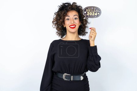 Photo for Young beautiful woman with curly hair wearing black dress over white studio background holding a Happy New year 2024 banner. - Royalty Free Image