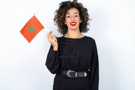 Photo for Young beautiful woman with curly hair wearing black dress and holding a Moroccan flag feeling confident and happy winner gesture. - Royalty Free Image