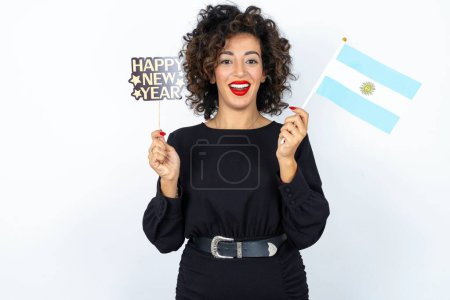 Photo for Young beautiful woman with curly hair wearing black dress, Argentinian flag and a Happy new year 2024 banner - Royalty Free Image