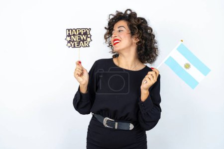 Photo for Young beautiful woman with curly hair wearing black dress, Argentinian flag and a Happy new year 2024 banner - Royalty Free Image