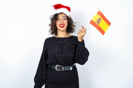 Téléchargez les photos : Jeune belle femme aux cheveux bouclés portant une robe noire et drapeau espagnol se sentant excité et confiant. - en image libre de droit