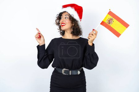 Téléchargez les photos : Jeune belle femme aux cheveux bouclés portant une robe noire et drapeau espagnol se sentant excité et confiant. - en image libre de droit
