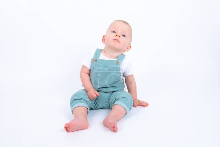 Photo for Studio portrait of cute little kid boy wearing green overall posing over white studio background - Royalty Free Image