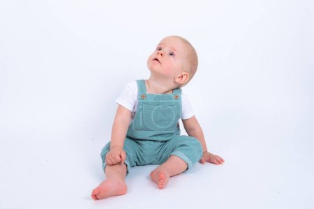 Téléchargez les photos : Portrait studio de mignon petit garçon portant globalement vert posant sur fond blanc studio - en image libre de droit