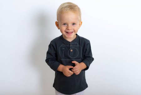Photo for Studio shot of happy blond kid boy wearing black t-shirt and white pants posing over white studio background - Royalty Free Image
