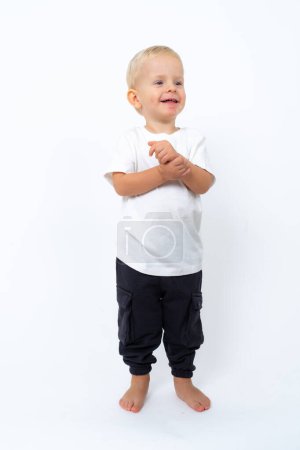 Photo for Portrait of beautiful blond kid boy wearing white t-shirt and black pants posing over white studio background - Royalty Free Image