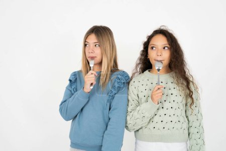 Photo for Very hungry multiracial group of girl friends over white studio background holding spoon into mouth dream of tasty meal - Royalty Free Image