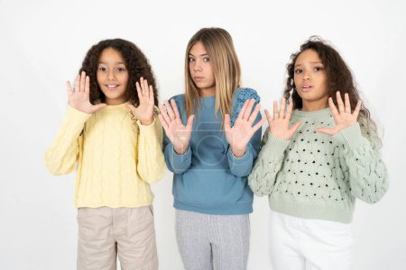 Foto de Tres chicas adolescentes alejándose de las manos palmas que muestran rechazo y negación con miedo y expresión repugnante. Detente y prohibido. - Imagen libre de derechos