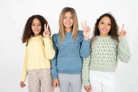 Foto de Tres chicas adolescentes mostrando y apuntando hacia arriba con los dedos número dos mientras sonríe confiado y feliz. - Imagen libre de derechos