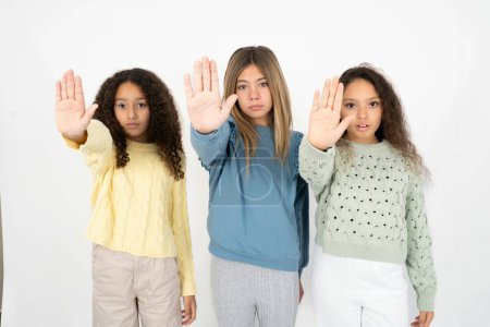 Téléchargez les photos : Trois adolescentes qui arrêtent de chanter avec la paume de la main. Expression d'avertissement avec geste négatif et sérieux sur le visage. - en image libre de droit