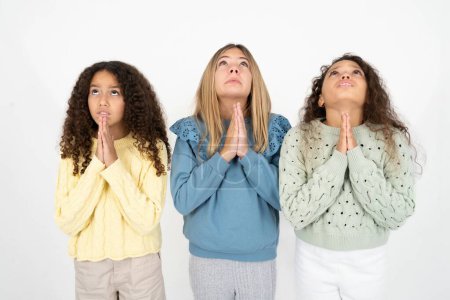 Téléchargez les photos : Trois adolescentes suppliant et priant avec les mains ainsi que l'expression de l'espoir sur le visage très émotionnel et inquiet. Mon Dieu ! - en image libre de droit