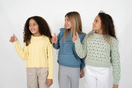 Foto de Tres chicas adolescentes Pareciendo orgullosas, sonriendo haciendo un gesto hacia un lado con el pulgar hacia arriba. Buen trabajo.! - Imagen libre de derechos