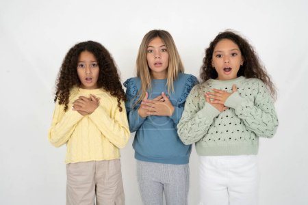 Scared three teenager girls looks with frightened expression, keeps hands on chest, being puzzled to notice something strange, People, hush reaction and emotions.