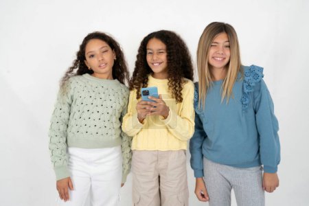 Foto de Emocionado tres chicas adolescentes guiño y ojo mantenga el uso del teléfono inteligente leer noticias de redes sociales - Imagen libre de derechos