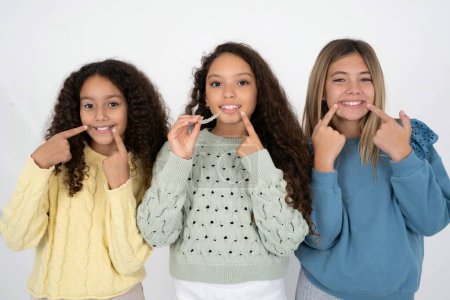 Foto de Tres chicas adolescentes sosteniendo un alineador invisible y señalando sus dientes rectos perfectos. Salud dental y concepto de confianza. - Imagen libre de derechos