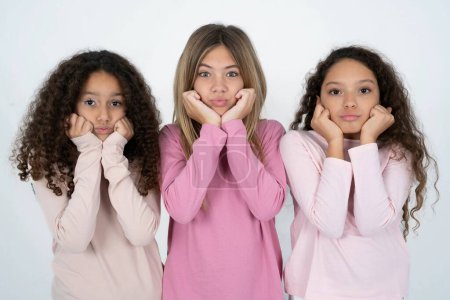 Photo for Three teenager girls with surprised expression keeps hands under chin keeps lips folded makes funny grimace - Royalty Free Image