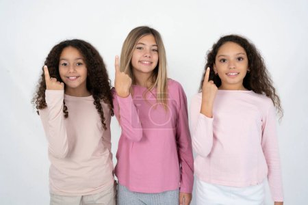 Foto de Tres chicas adolescentes sonriendo y mirando amigable, mostrando el número uno o primero con la mano hacia adelante, cuenta atrás - Imagen libre de derechos