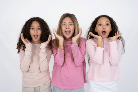 Surprised happy three teenager girls , glad to see big discounts on clothes, expresses shock, keeps hands near head, jaw dropped.