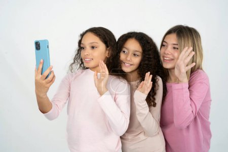 Téléchargez les photos : Trois adolescentes tient téléphone portable moderne et fait ondes d'appel vidéo palme dans le geste bonjour. Personnes concept de technologie moderne - en image libre de droit