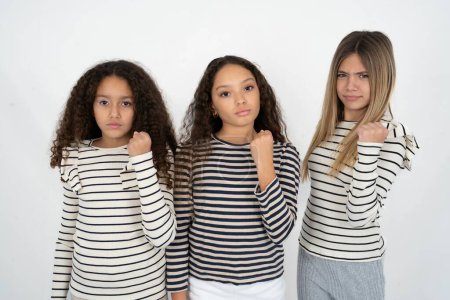 Photo for Three teenager girls shows fist has annoyed face expression going to revenge or threaten someone makes serious look. I will show you who is boss - Royalty Free Image