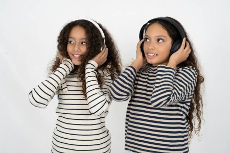 Téléchargez les photos : Groupe multiracial de filles amies sur fond de studio blanc porte casque stéréo écoute de la musique concentrée de côté. Les gens hobby concept de style de vie - en image libre de droit