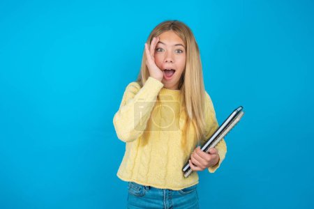 Photo for Beautiful kid girl wearing yellow sweater over blue background with scared expression, keeps hands on head, jaw dropped, has terrific expression. Omg concept - Royalty Free Image