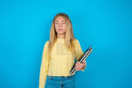 Photo for Beautiful kid girl wearing yellow sweater over blue background looking sleepy and tired, exhausted for fatigue and hangover, lazy eyes in the morning. - Royalty Free Image