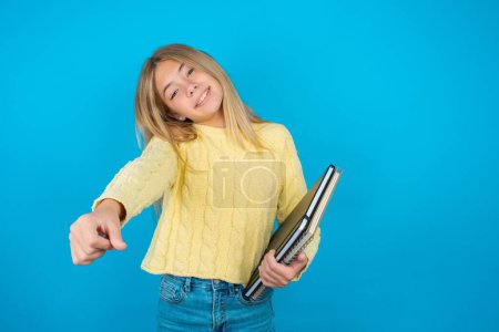 Photo for Beautiful kid girl wearing yellow sweater over blue background imagine steering wheel helm rudder passing driving exam good mood fast speed - Royalty Free Image
