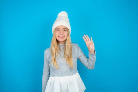 Photo for Beautiful kid girl wearing white knitted hat and blue sweater showing and pointing up with fingers number four while smiling confident and happy. - Royalty Free Image