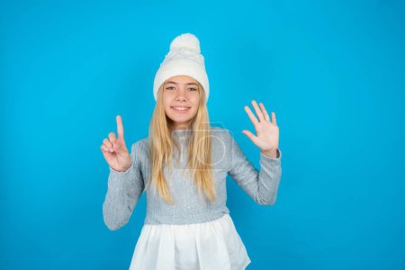 Photo for Beautiful kid girl wearing white knitted hat and blue sweater showing and pointing up with fingers number six while smiling confident and happy. - Royalty Free Image