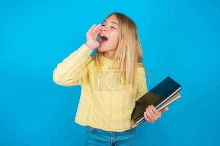 Photo for Beautiful kid girl wearing yellow sweater over blue background shouting and screaming loud to side with hand on mouth. Communication concept. - Royalty Free Image