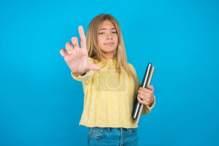 Photo for Beautiful kid girl wearing yellow sweater over blue background making fun of people with fingers on forehead doing loser gesture mocking and insulting. - Royalty Free Image