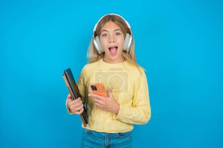 Photo for Beautiful kid girl wearing yellow sweater over blue background holding in hands showing new cell, - Royalty Free Image