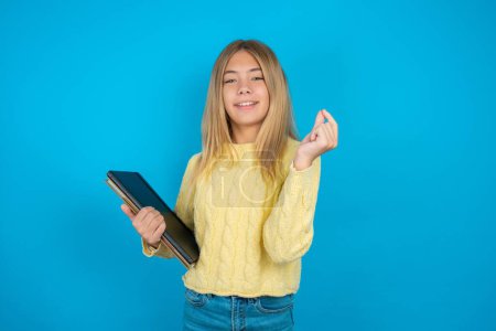Foto de Hermosa niña vistiendo suéter amarillo sobre fondo azul apuntando hacia arriba con la mano que muestra hasta siete dedos gesto en chino lenguaje de signos Q. - Imagen libre de derechos