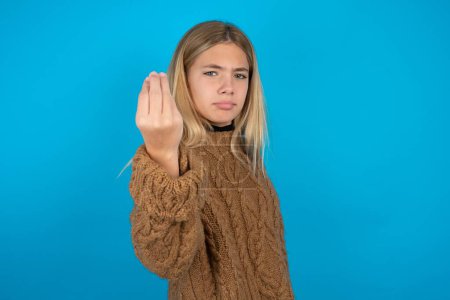 Téléchargez les photos : Blonde enfant fille portant brun tricoté pull sur fond bleu Faire geste italien avec la main et les doigts expression confiante - en image libre de droit