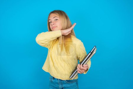 Photo for Beautiful kid girl wearing yellow sweater over blue background cutting throat with hand as knife, threaten aggression with furious violence. - Royalty Free Image